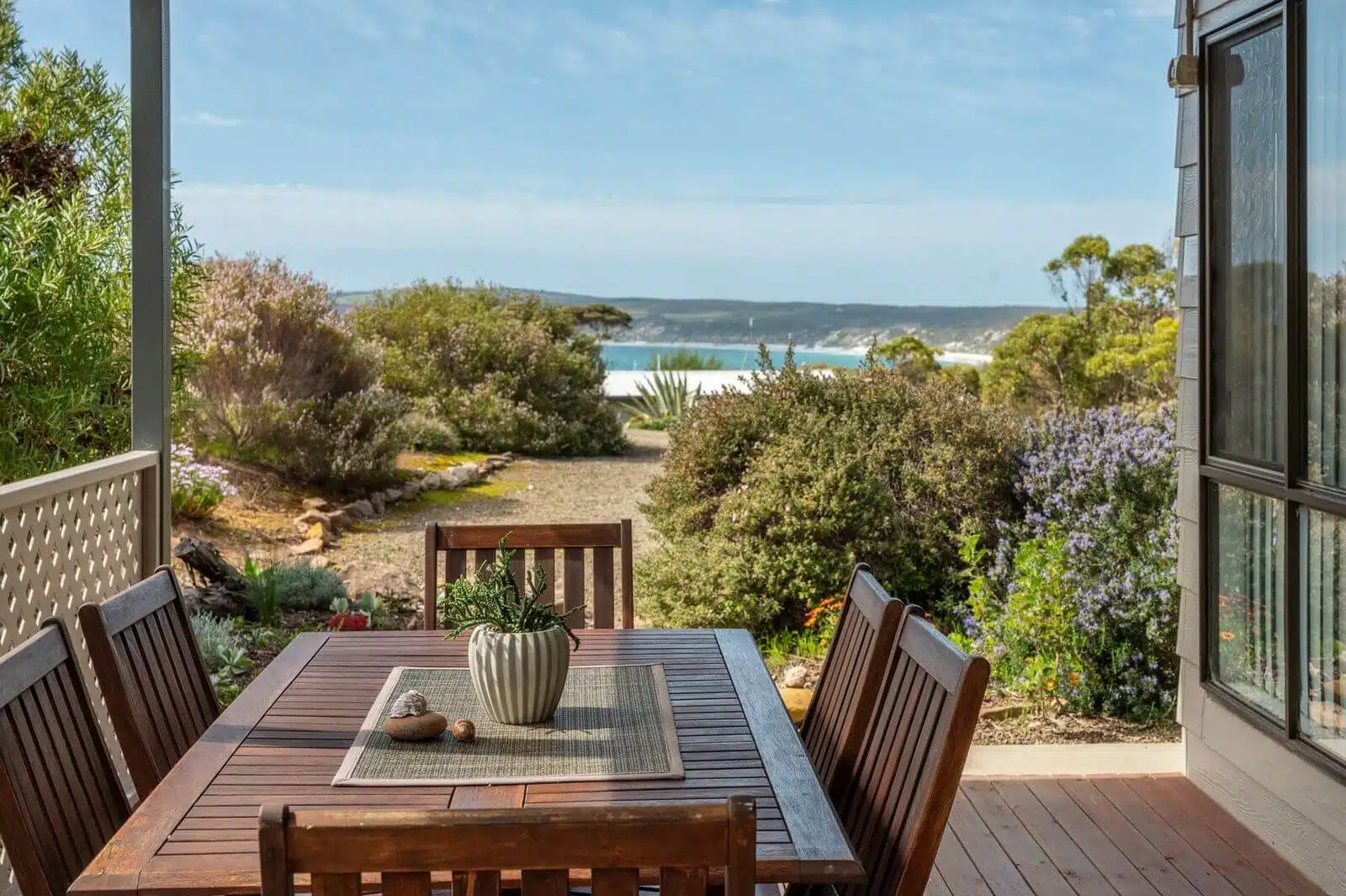A serene patio at Shalom House, holiday home in Emu Bay, Kangaroo Island with comfortable outdoor furniture surrounded by birds chirping and koalas in the trees, overlooking a tranquil bay.